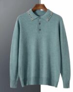 Photo d'un pull polo bleu avec col à liseré au milieu et trois boutons sur un cintre en bois marron foncé le tout devanyt un mur bicolore blanc à droite et gris à gauche