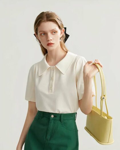 Une jeune femme portant un polo beige avec une jupe verte. Sac à la main