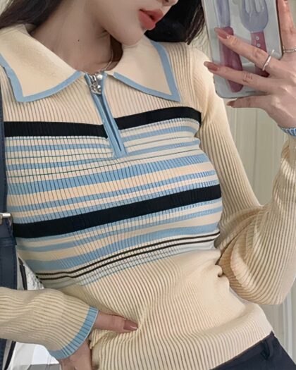 Polo à manches longues beige à rayures bleues claires et bleues foncée. Porté par une femme qui regarde son téléphone