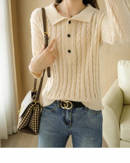 Photo d'une jeune femme debout dans un salon au canapé blanc et portant un pull polo blanc à boutons noirs sur un jean bleu ceinture foncée à boucle et un sac chiné en bandoulière