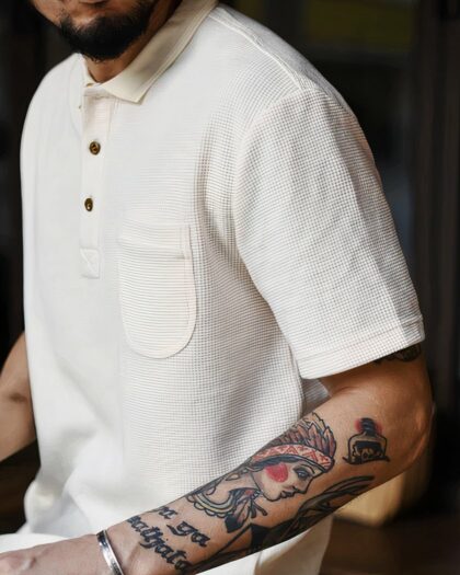 Photo d'un homme portant un polo vintage en nid d'abeille blanc avec un tatouage sur le bras.