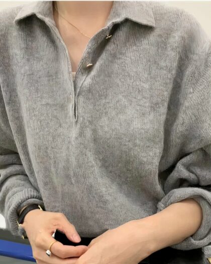 Photo d'une femme portant un pull polo gris en laine avec col et boutonnage style polo, manches longues relevées, un sac à main noir au bras gauche