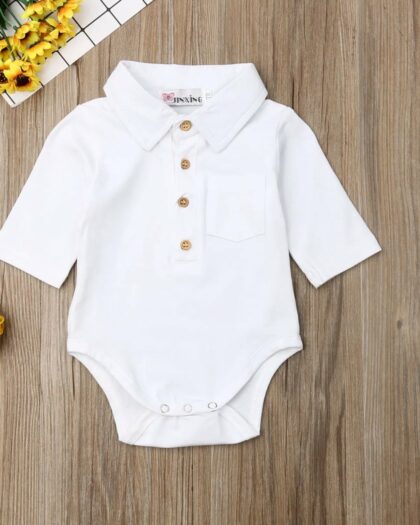 On voit un body polo blanc pour bébé sur fond en bois.