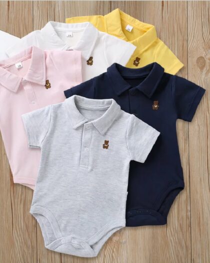 On voit cinq bodys polos pour bébé : un jaune, un blanc, un rose, un bleu et un gris. Ils sont présentés sur du bois.