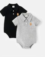 On voit deux polos body pour bébé. Un noir et un gris, il sont un écusson en forme de tête d'ourson brodé sur la poitrine.