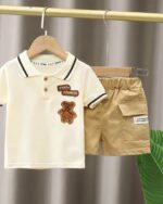 On voit un polo manches courtes beige pour bébé et le short assorti, sur une tringle.