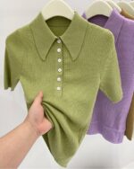 Polo à manches courtes vert avec des boutons suspendu sur un sintre et soulevé par une main