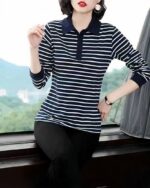 Polo à manches longues rayé bleu et bmanc porté par un femme positionnée davant une fenêtre