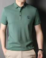 Homme portant un polo brodé vert sur un fond gris.