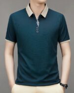 Homme portant un polo bleu à manches courtes et col beige sur fond gris.