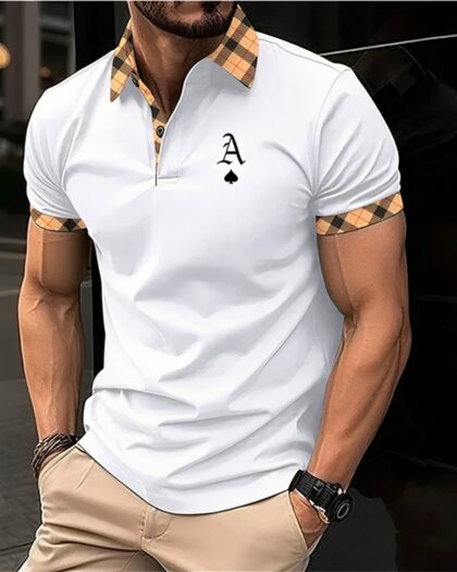 Photo d'un homme adossé à un mur de verre noir les mains dans les poches d'un pantalon beige et portant un polo de golf blanc avec une lettre noire sur la poitrine et des ornements à carreaux autour des manches courtes, au col et à la patte de boutonnage