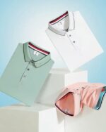 Photo représentant trois polos de sport pliés en équilibre sur des cubes blancs le polo blanc en haut, le vert juste en dessous et le rose est posé col en bas sur le cube de droite le tout sur un fond bleu ciel