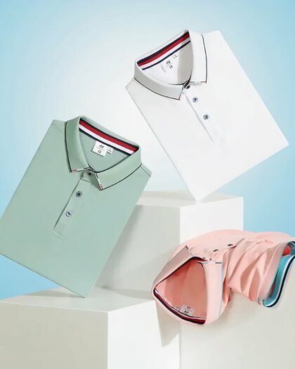 Photo représentant trois polos de sport pliés en équilibre sur des cubes blancs le polo blanc en haut, le vert juste en dessous et le rose est posé col en bas sur le cube de droite le tout sur un fond bleu ciel