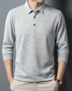 Homme portant un polo à manches longues gris sur un fond gris foncé.