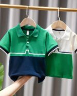 On voit deux polos vert et blanc pour bébé garçon suspendus à une tringle.