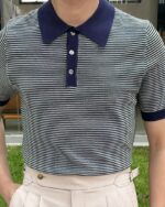 Photo d'un polo marinière à fines rayures porté par un homme avec un pantalon beige, une main dans une poche.