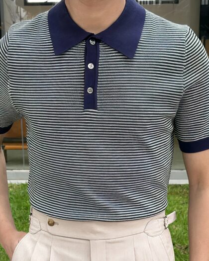 Photo d'un polo marinière à fines rayures porté par un homme avec un pantalon beige, une main dans une poche.