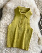 Photo d'un polo sans manche jaune dos nu tricot côtelé posé sue un tapis en fausse fourrure blanche sur un sol gris et un petit sac bandoulière en perles blanches à côté