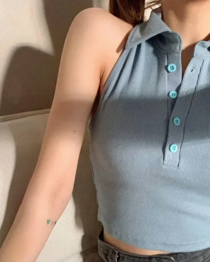 Photo d'une jeune femme assise dans un fauteuil crème et portant un polo sans manche court bleu à cinq boutons semblant être dos nu