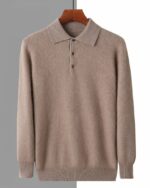 Photo d'un pull polo marron avec col chemise et boutons , manches resserrées au bout sur une cintre marron foncé en bois le tout sur un fond blanc à droite et gris à gauche