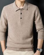 Photo d'un homme debout els mains dans les poches de son pantalon beige portant un pull polo en laine marron clair à boutons noirs, manches relevées sur l'avant-bras une montre au poignet gauche