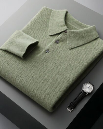 Photo d'un pull polo vert plié dans une boîte noire ouverte posée sur un meuble gris foncé avec une montre juste à côté