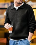 Photo d'un homme portant un pull polo vintage en maille sans boutons par dessus un t-shirt blanc avec un jean. L'homme à une main dans la poche et tient un verre de l'autre main.