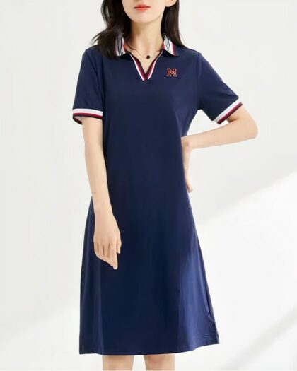 Photo d'une jeune femme debout une main à la taille portant une robe polo bleu marine avec col, décolleté et bord des manches tricolores le tout devant un mur bleu pâle à rays de lumière blanche