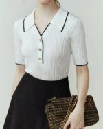 Photo d'une femme portant un polo vintage en tricot côtelé blanc à détail noir avec une jupe et un sac pochette à la main.