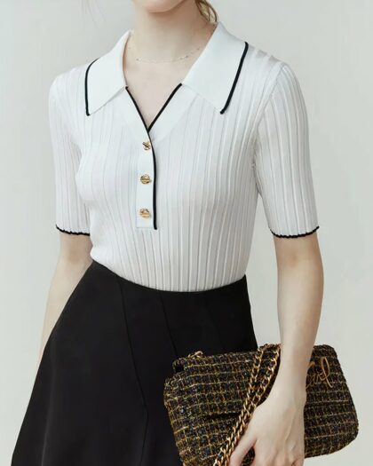 Photo d'une femme portant un polo vintage en tricot côtelé blanc à détail noir avec une jupe et un sac pochette à la main.