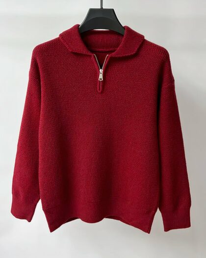Photo d'un pull polo zippé bordeaux présenté sur un cintre en bois foncé le tout sur un fond gris bleuté