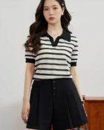 Photo d'une femme portant un polo vintage rayé en tricot sans boutons avec une jupe noir devant un buffet en bois.