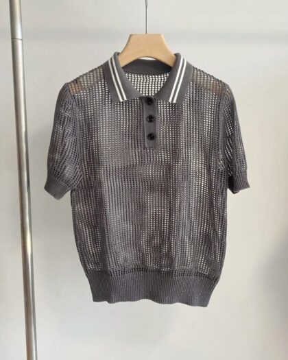 Photo d'un polo gris ajouré à manches courtes et col bicolore gris et blanc sur un cintre en bois clair suspendu à un portant en acier le tout sur un fond gris clair