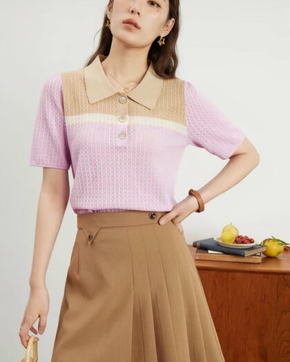 Photo d'une femme portant un polo vintage en tricot texturé rose et beige avec une jupe camel devant un meuble en bois.