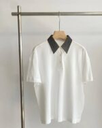 Photo d'un polo chic blanc à col gris pour femme sur un cintre en bois clair lui-même sur un portant en acier, le tout sur un fond gris clair