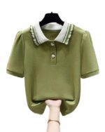 Phot d'un polo à manches courtes vert à col blanc et bandes vertes avec boutons en forme de coeurs blancs sur un cintre noir relevé en bas par une main féminine