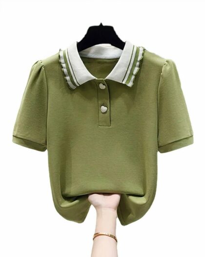 Phot d'un polo à manches courtes vert à col blanc et bandes vertes avec boutons en forme de coeurs blancs sur un cintre noir relevé en bas par une main féminine