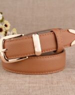 Ceinture fine pour femme de couleur camel avec une boucle doré, enroulée sur elle même avec des fleurs en arrière plan.