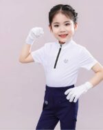 Une petite fille porte un polo blanc zippé avec des gants blancs et un pantalon bleu marine