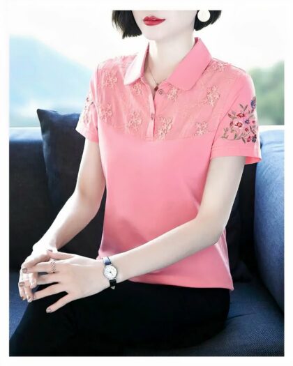 Photo d'une femme assise, un gros coussin derrière elle, et portant un bas foncé avec un polo rose à empiècement brodé 3D te broderies fleurs sur la manche, derrière elle un panorama flou de nature