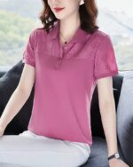 Photo montrant une femme assise dos à une fenêtre un gros coussin noir derrière elle et portant un polo rose fonce à empiècement et manches évidés et un pantalon blanc