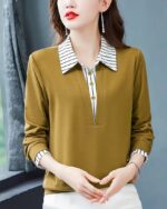 Photo d'une femme debout dos à une fenêtre portant un bas blanc cassé et un polo kaki manches longues très chic à rayures blanches et kaki au bord des manches et au col et patte de boutonnage