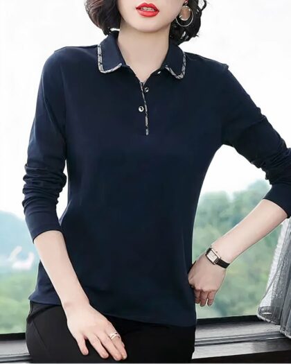 Photo d'une femme assise sur le rebord d'une fenêtre portant un pantalon noir et un polo chic bleu marine à manches longues avec liseré fin au col et en bord de patte de boutonnage