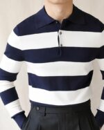 Photo d'un homme portant un polo vintage marinière à manches longues avec un pantalon noir taille haute élégant, les mains dans les poches devant un mur beige.