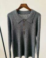 Photo d'un pull polo gris foncé à manches longues, col polo et boutons sur un cintre en bois foncé le tout sur fond gris clair