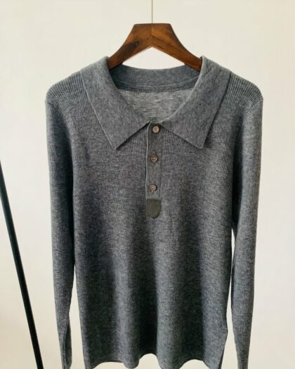 Photo d'un pull polo gris foncé à manches longues, col polo et boutons sur un cintre en bois foncé le tout sur fond gris clair