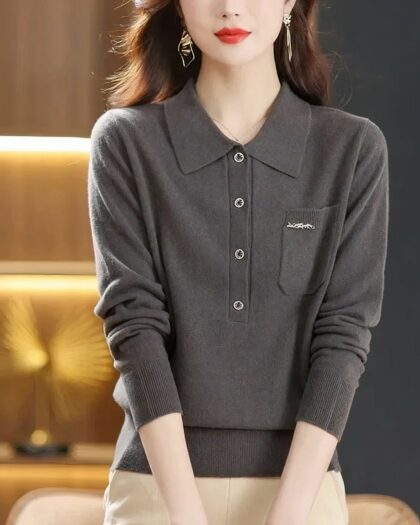 Photo d'une femme debout mains devant portant un pantalon beige et un pull polo gris foncé avec une poche poitrine ornée d'un petit écusson clair le tout sur un fond éclairage doré sur la gaucheet noir à droite