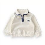 Polo blanc zippé avec un liseré bleu autour du col et du zip. Il y a une broderie avec un un petit chien et "hapiness" écrit