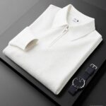 Polo zippé blanc plié sur une table noir avec une montre noir posée à coté.