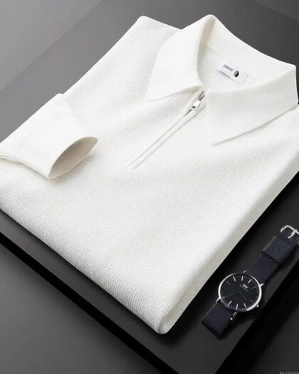 Polo zippé blanc plié sur une table noir avec une montre noir posée à coté.